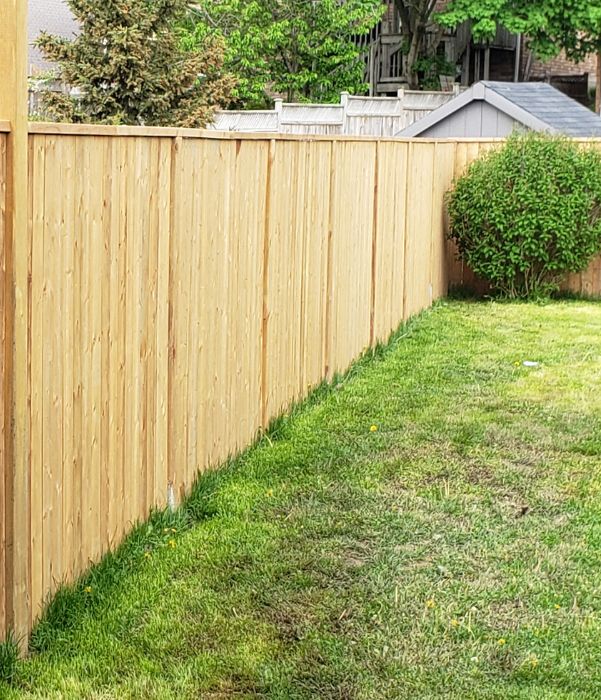 A wooden fence encloses a backyard, featuring a well-maintained green lawn.